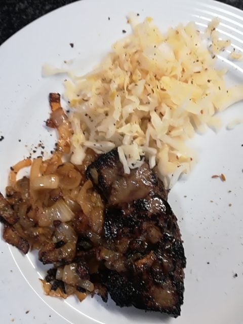 A white plate with a serving of grilled meat topped with caramelized onions, alongside shredded cheese—perfect for keto weight loss. A sprinkle of ground black pepper adds extra flavor to this satisfying, low-carb meal.