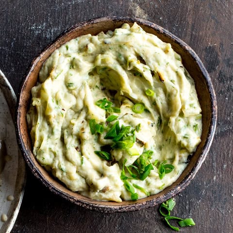 A rustic bowl filled with creamy, keto weight loss-friendly mashed potatoes garnished with chopped green onions, placed on a dark wooden surface.