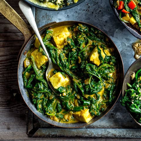 A skillet filled with creamy spinach and paneer curry—a keto weight loss dish—features vibrant green spinach leaves and golden paneer cubes in a rich, spiced sauce, with a spoon resting inside.