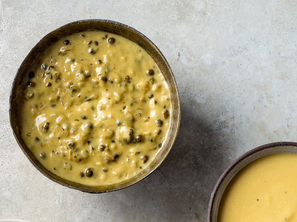 A bowl of creamy yellow curry with visible spices and herbs sits on a light stone surface, next to another bowl partially filled with smooth yellow soup—an inviting meal perfect for keto weight loss enthusiasts.