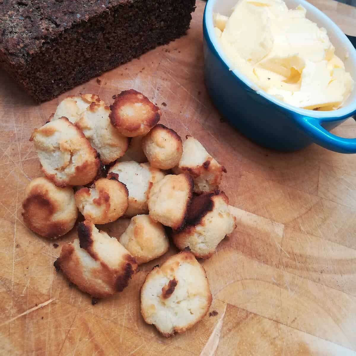 A loaf of dark bread, a small pile of round, golden-brown keto weight loss cookies, and a blue dish filled with butter sit on a wooden board.
