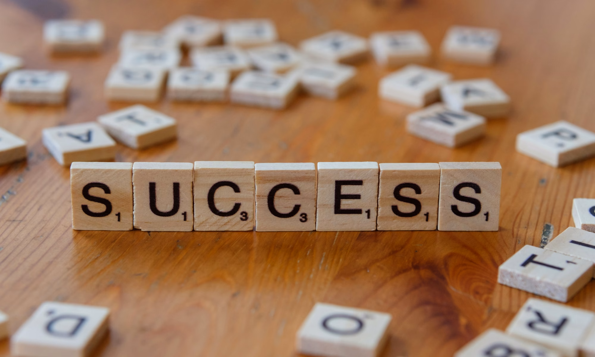 Wooden letter tiles spelling SUCCESS are arranged in a row on a wooden table, with more scattered tiles in the background—reminding you that you don’t need another diet plan to achieve your goals.